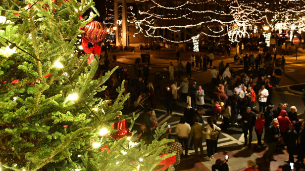 A crowd surrounds a large Chistrmas tree in a downtown market square