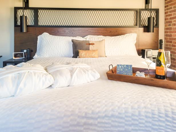 Bed with white bedding, two white bathrobes, a tray with two glasses and a bottle of prosecco