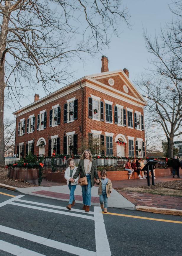 Woman with children crossing street with historic building and holiday decorations in background