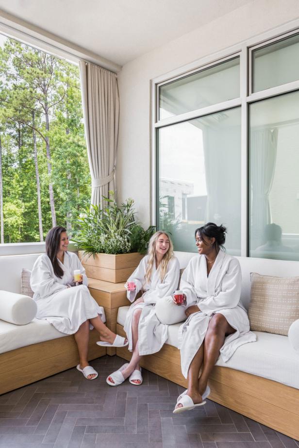 three women in white bathrobes smiling at each other with drinks