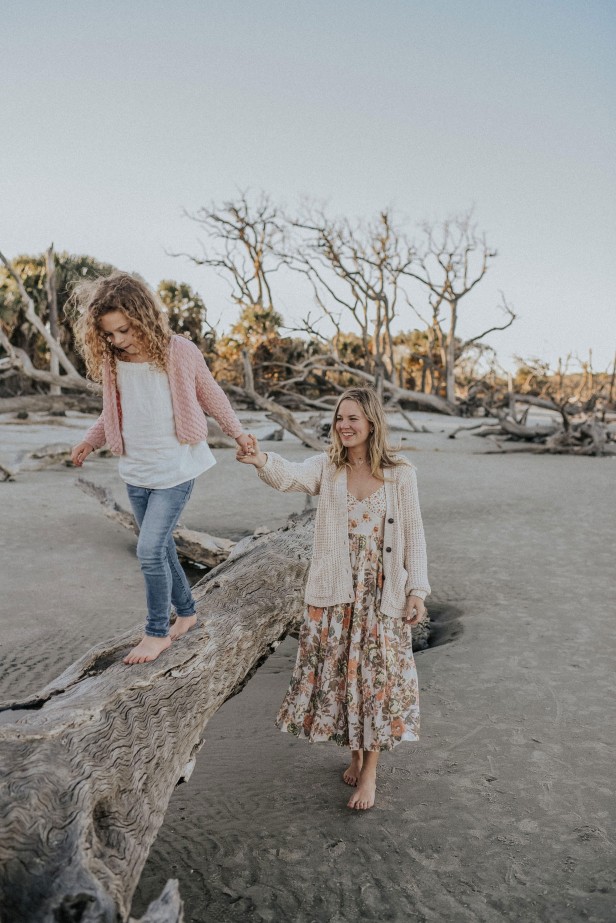 Young girl walking on fallen tree holding her mother's hand on Driftwood Beach on Jekyll Island, Georgia