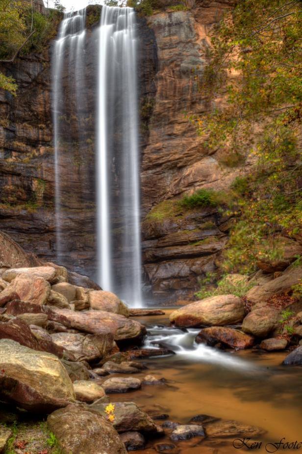 A tall waterfall streams down into a rocky riverbed.