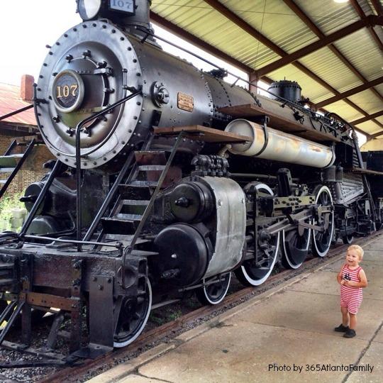 A small child looks up at a large train engine sitting in the station.