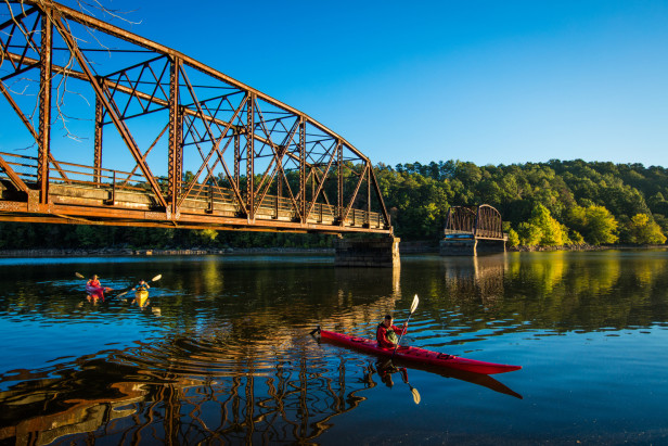 A kayak floats under a bridge stretching across a river.