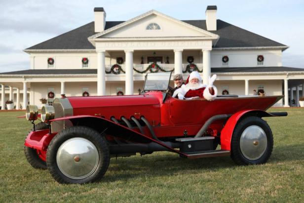 Santa driving a shiny red antique car.