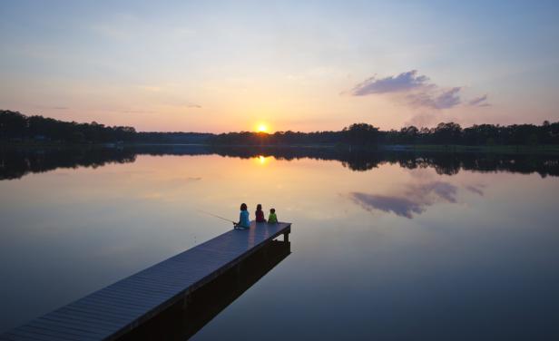 Three people sitting at the end of a dock fishing in a lake