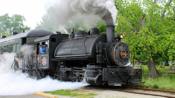 Steam puffs from a black train chugging along the tracks.