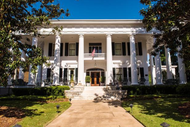 A historic mansion with large columns is framed by giant trees