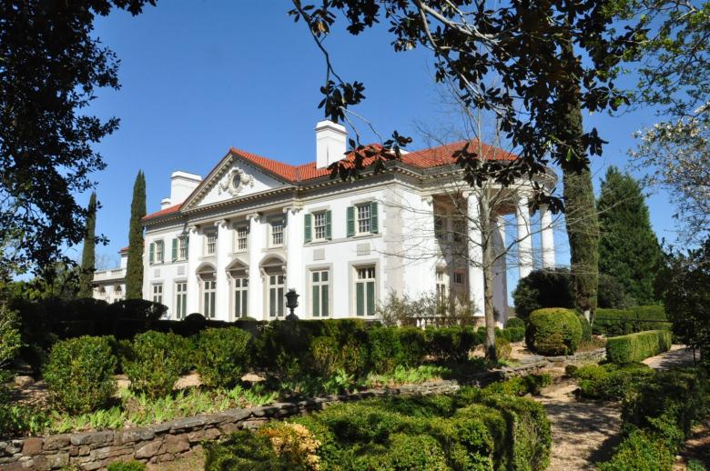 A large white mansion is framed by tall trees on each side.