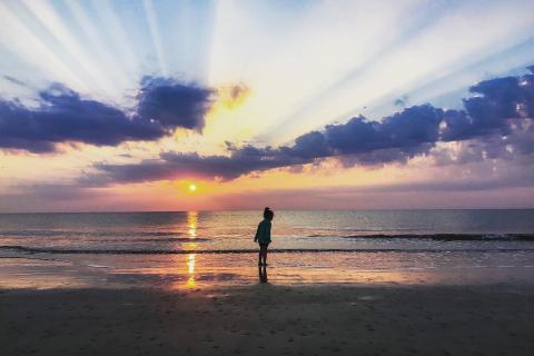 A child runs on the beach while the sun sets over the ocean behind them on a Jekyll Island, Georgia, beach.