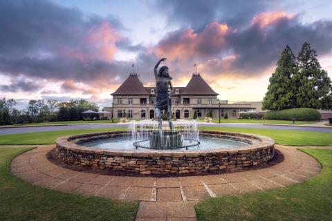Sunset image of a fountain with statue woman dancing in the water in front of a mansion