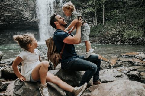 A father and two children splash in the water with a waterfall in the background. 