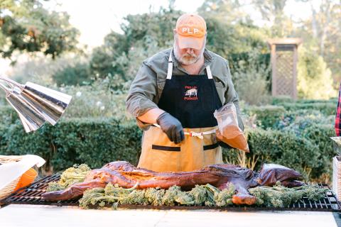 A man stands over the grill at a pig roast