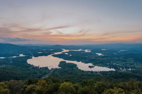 Aerial view of a large lake surrounded by trees with a sunset in the background