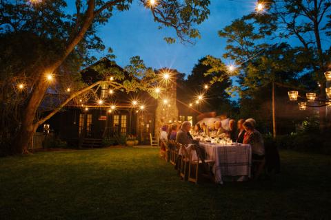 Large group dining at a long table outside under trees and string lights