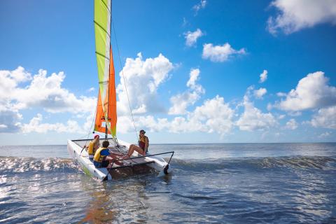 Family wearing life jackets and boating on a sunny day in the water with clouds above them.