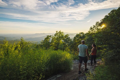 A couple hiking on a trail surrounded with lush greenery.