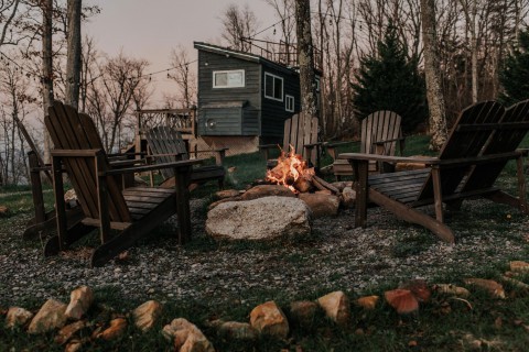 seven wooden Adirondack chairs around a fire pit with a tiny house rental in Rising Fawn, Georgia, in the background