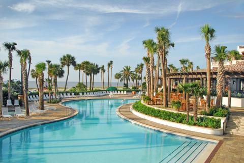 A pool winds through an outdoor resort area surrounded by palm trees.