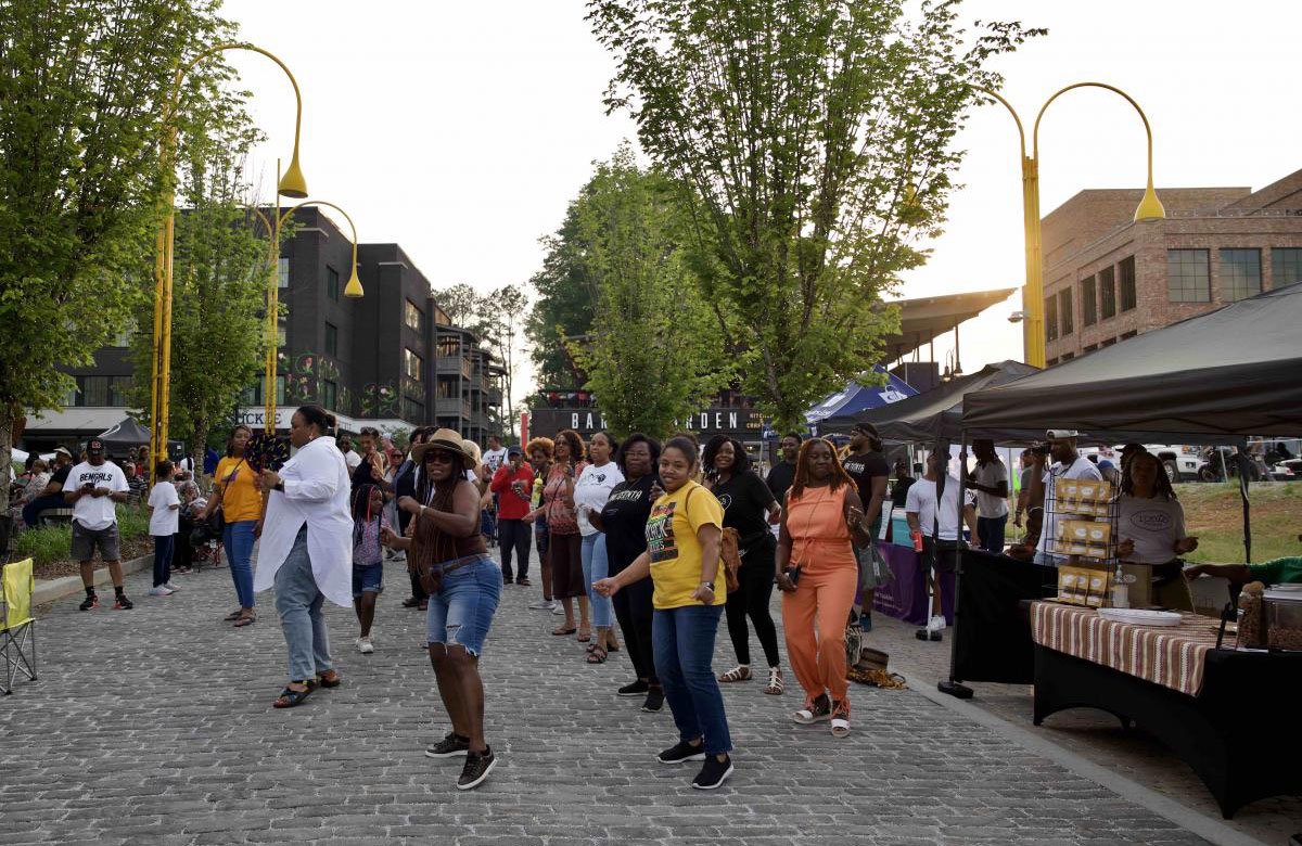 Group of women dancing in a street with vendor booths along the side