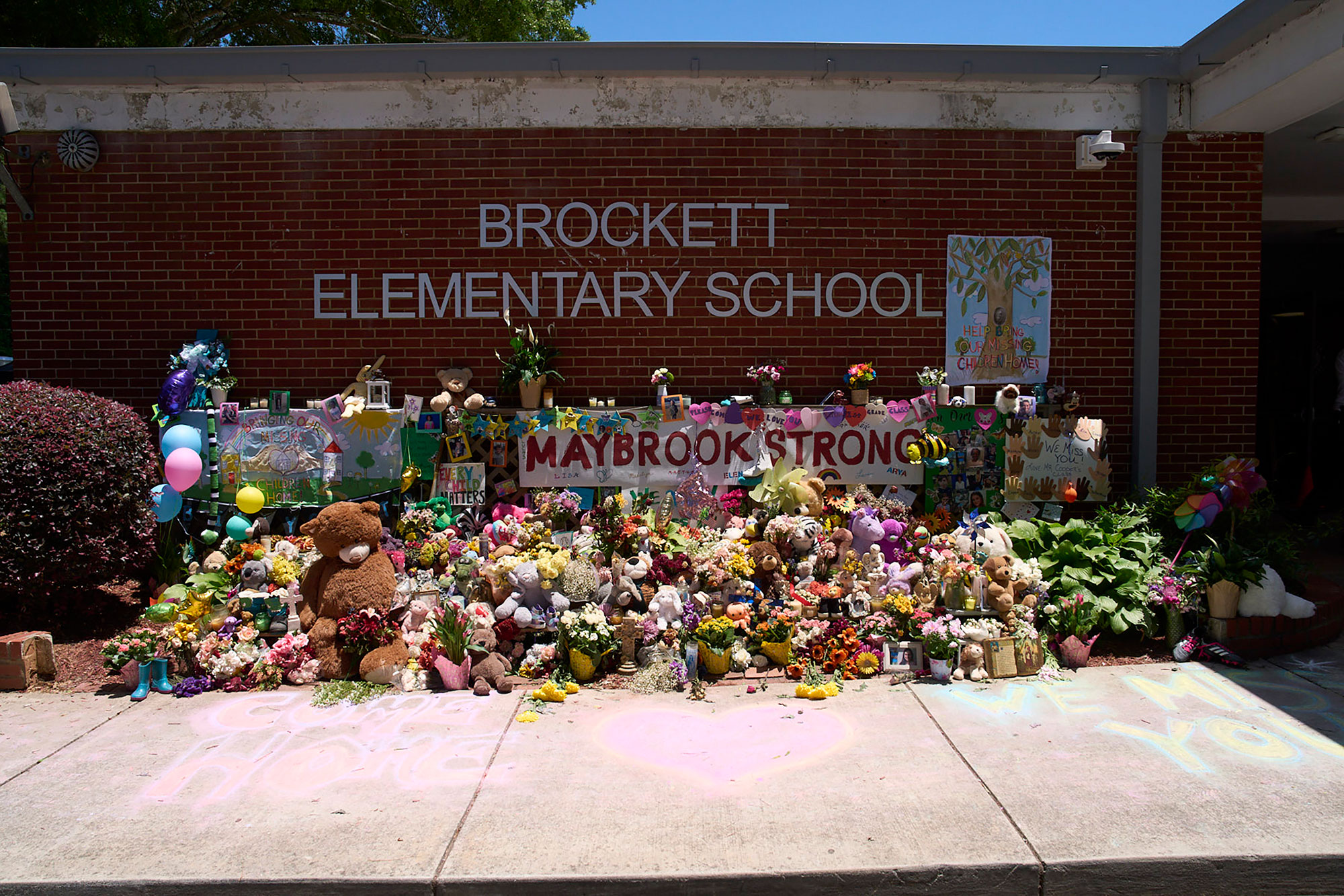 A memorial of flowers and stuffed animals in front of the sign for Brockett Elementary in Tucker, Georgia